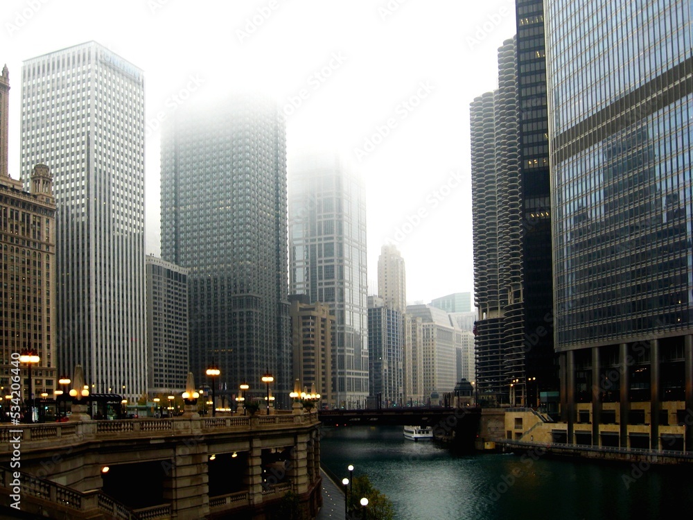 Obraz premium Chicago in November. the Chicago River. skyscrapers and bridge. tour boat on the canal. foggy scene.. yellow street lights. office towers reflecting in silver glass exterior curtain walls