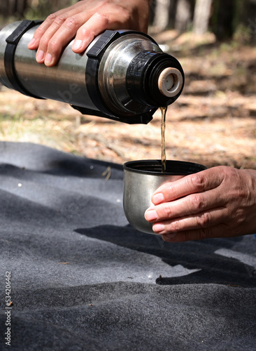 women's hands pour tea from a thermos in the forest on a picnic