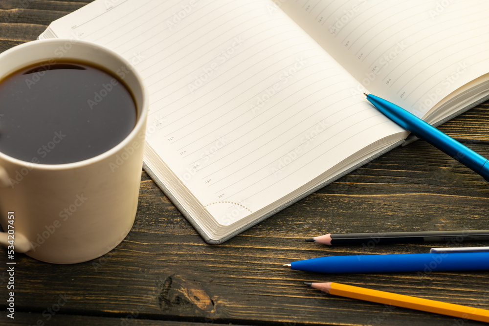 mug of coffee on the table next to the diary with a pen and pencil in the morning mug of coffee on the table next to the diary with a pen and pencil in the morning