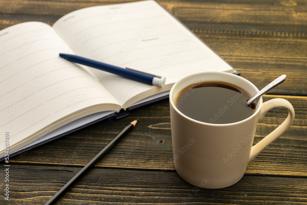 mug of coffee on the table next to the diary with a pen and pencil in the morning mug of coffee on the table next to the diary with a pen and pencil in the morning