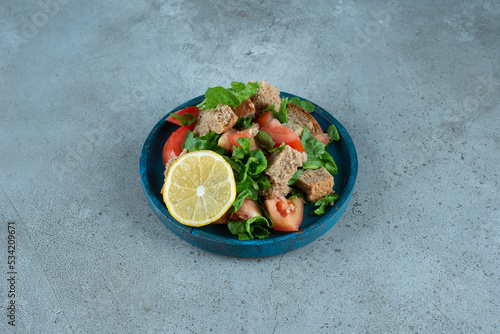 Sliced tomato, bread, lemon and greens on blue plate