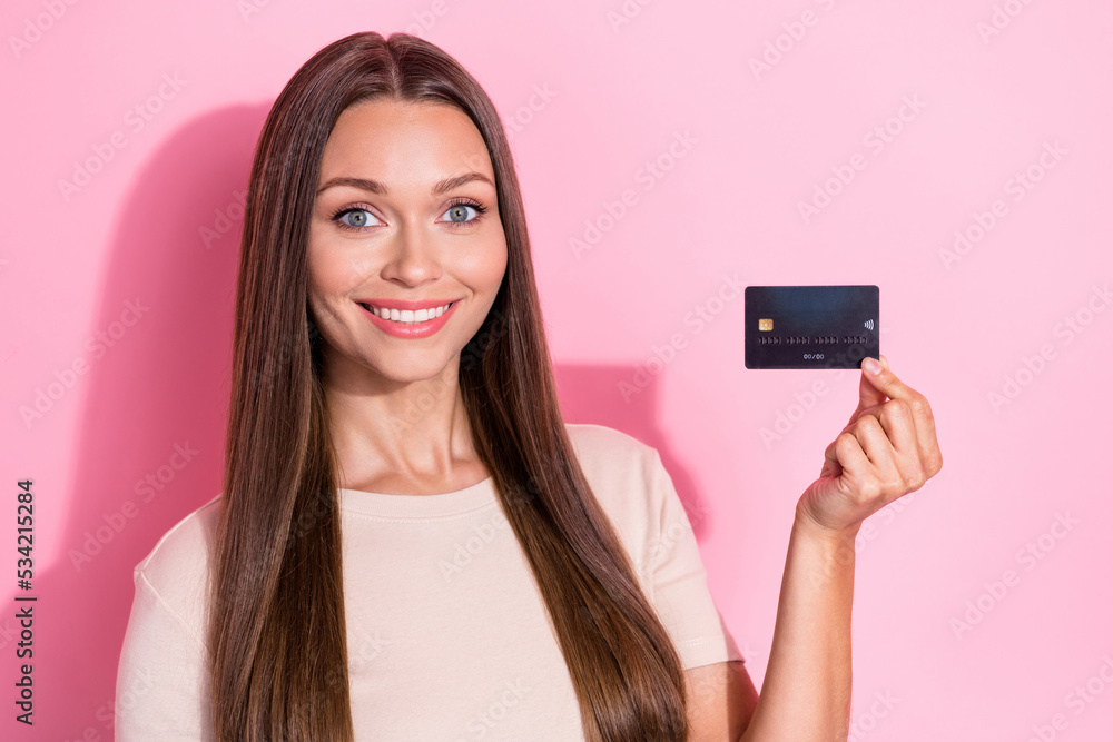 Photo of positive nice girl arm hold debit plastic card beaming smile isolated on pink color background Photo of positive nice girl arm hold debit plastic card beaming smile isolated on pink color background
