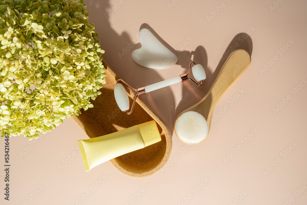 A face roller and quartz massager in the form of the heart, a face brush and a face serum with vitamin C lying on the beige background A face roller and quartz massager in the form of the heart, a face brush and a face serum with vitamin C lying on the beige background