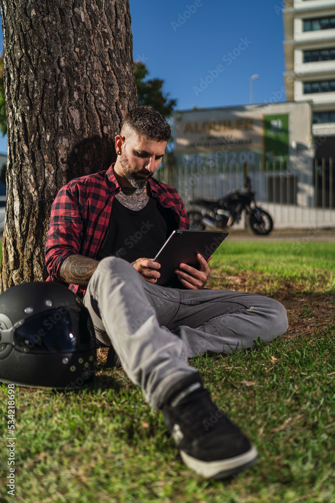 Chico joven tatuado con barba dibujando en tablet digital con su motocicleta de fondo Chico joven tatuado con barba dibujando en tablet digital con su motocicleta de fondo