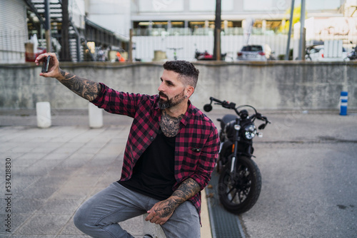 Chico con camisa a cuadros roja posando con su casco de moto y la motocicleta