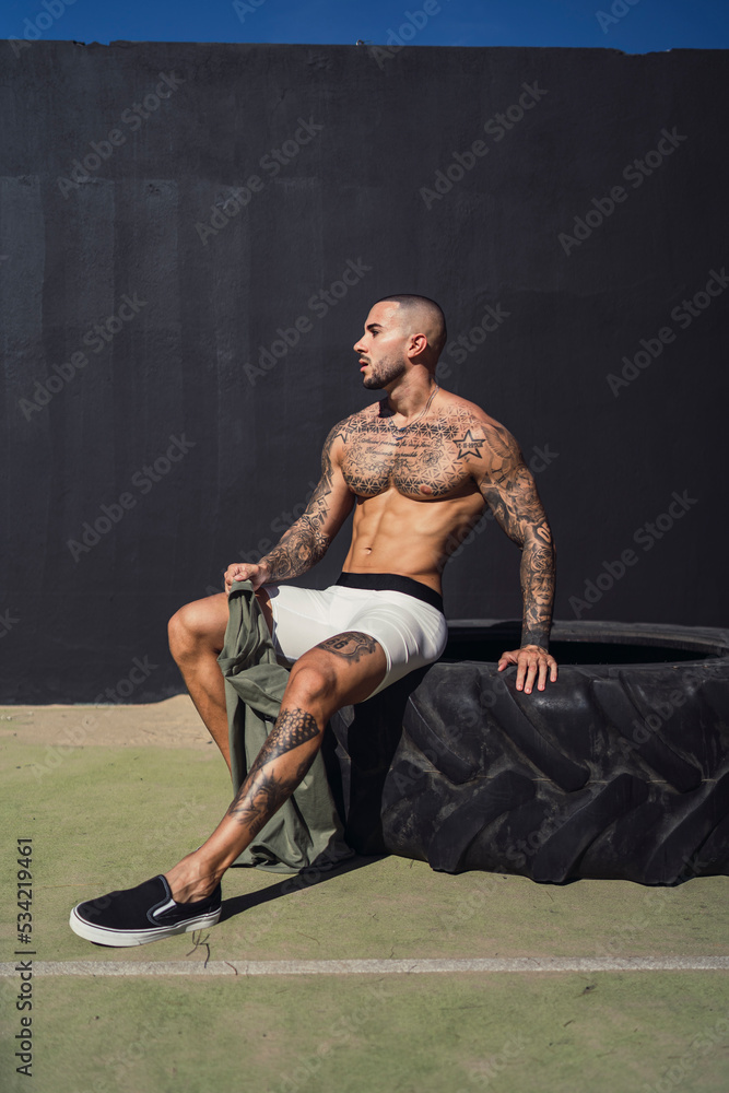 Chico joven tatuado y musculoso posando y haciendo ejercicio en gimnasio al aire libre en día soleado