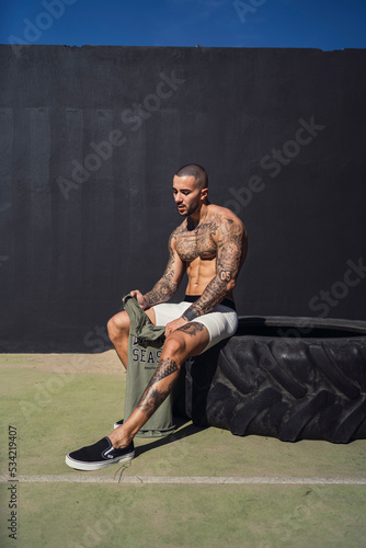 Chico joven tatuado y musculoso posando y haciendo ejercicio en gimnasio al aire libre en d  a soleado