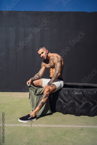 Chico joven tatuado y musculoso posando y haciendo ejercicio en gimnasio al aire libre en día soleado