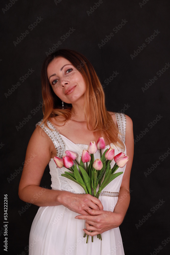 Portrait of beautiful woman in white dress with a bouquet of tulips on black background Portrait of beautiful woman in white dress with a bouquet of tulips on black background
