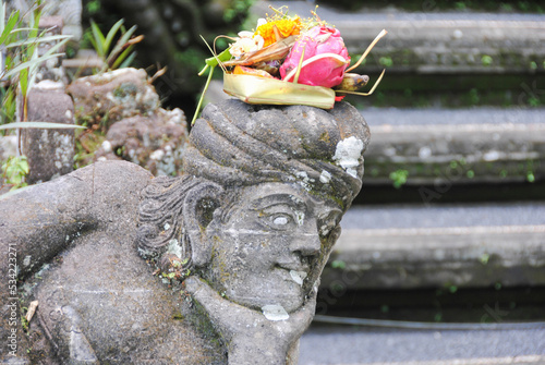 Balinese religious offering (canang sari) over a stone statue. Bali, Indonesia