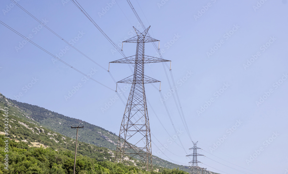 High voltage electric pylons at Greek forest mountain background. Energy transmission concept.