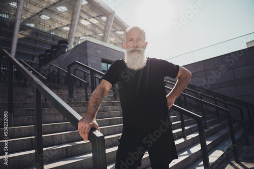 Portrait of attractive virile masculine sportive grey-haired man working out on fresh air on stairs outdoors