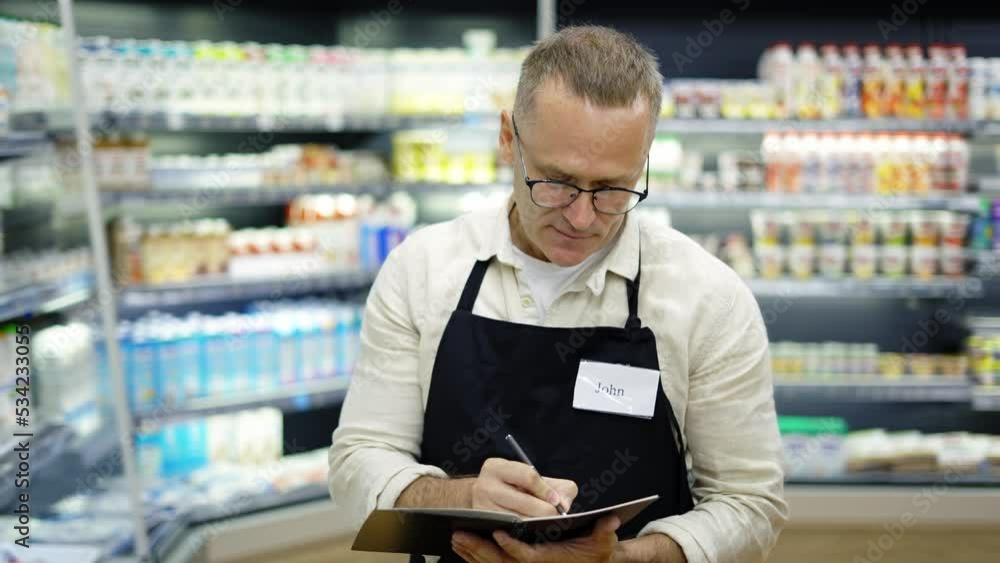 Portrait of a sales assistant in glasses with a notebook and a pencil in his hands in a grocery store. The concept of work in the store. Weekdays Portrait of a sales assistant in glasses with a notebook and a pencil in his hands in a grocery store. The concept of work in the store. Weekdays
