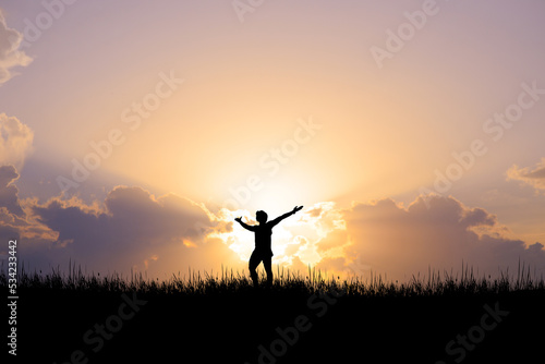 Silhouette of a man standing with his hands up. happily in the meadow