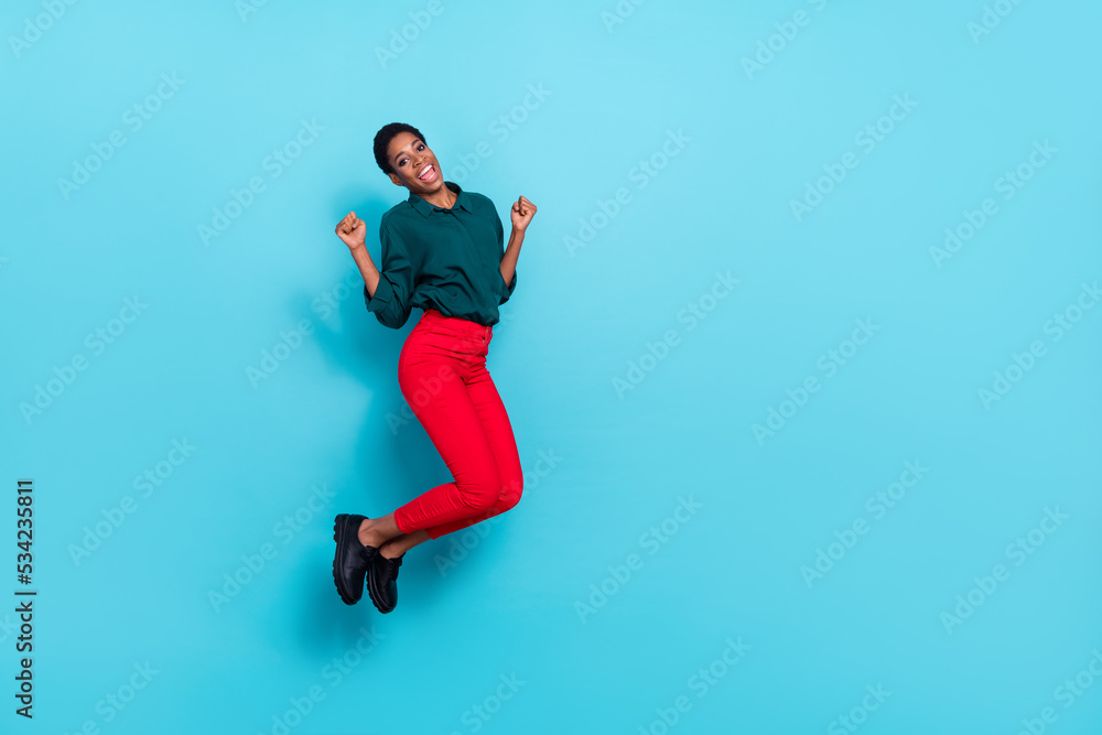 Photo of funny lucky trans person dressed green shirt jumping high rising fists empty space isolated blue color background