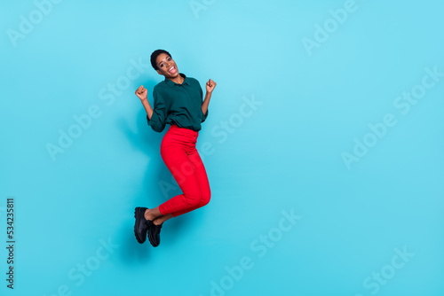 Photo of funny lucky trans person dressed green shirt jumping high rising fists empty space isolated blue color background