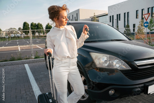 Stylish middle aged businesswoman holding travel bag looking at keys standing near new car  © Maria Vitkovska