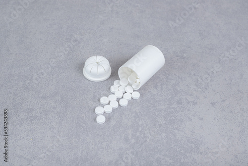 A small white jar of white pills on gray background