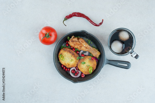 A dark pan with fried chicken and potato on whie background