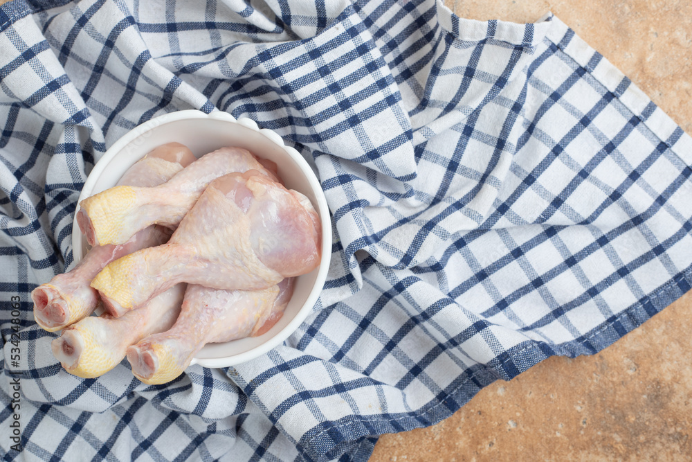 Unprepared chicken legs in white plate on tablecloth