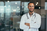 Portrait of young happy and smiling doctor, man in medical coat and stethoscope smiling and looking at camera, Arab doctor with crossed arms working inside modern clinic office.
