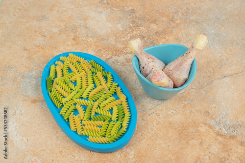 Unprepared spiral macaroni with chicken legs on blue plate