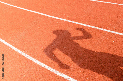The shadow of man who show extend the arms on red running race track in sport stadium,abstract background, winner sport concept.