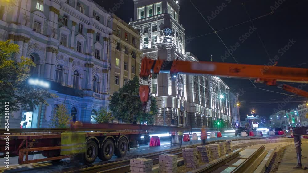 Orange construction telescopic mobile crane unloading tram rails from truck night timelapse. Industrial workers with hardhats and uniform. Reconstruction of tram tracks in the city center Orange construction telescopic mobile crane unloading tram rails from truck night timelapse. Industrial workers with hardhats and uniform. Reconstruction of tram tracks in the city center