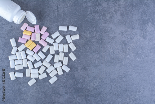 Small plastic bottle fallen over next to a pile of gum on marble background