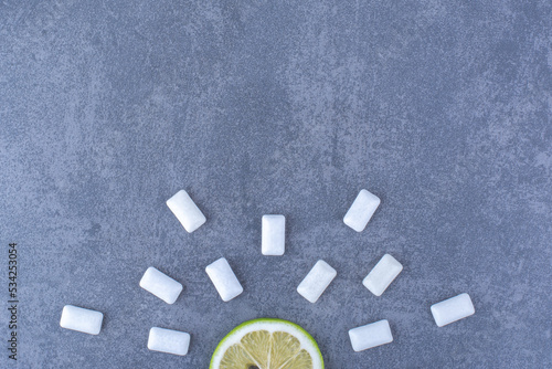 Chewing gum tablets lined around a sliced of lemon on marble background