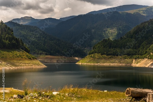 Closeup shot of the Gura Apelor dam in Romania, surrounded by green plants and a mountain range photo