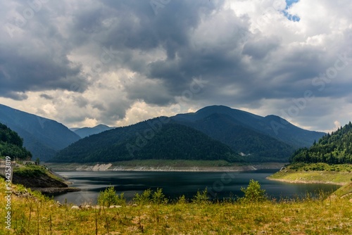 Closeup shot of the Gura Apelor dam in Romania, surrounded by green plants and a mountain range photo