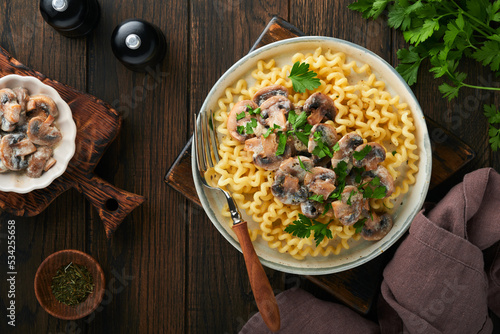 Fusilli pasta with mushrooms, cheese and garlic creamy sauce on plate on old wooden dark table background. Top view. Traditional Italian cuisine.