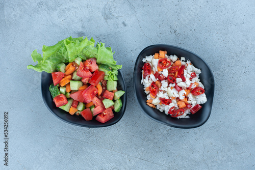 Bowl of shepherd's salad next to a bowl of pepper and cauliflower salad on marble background