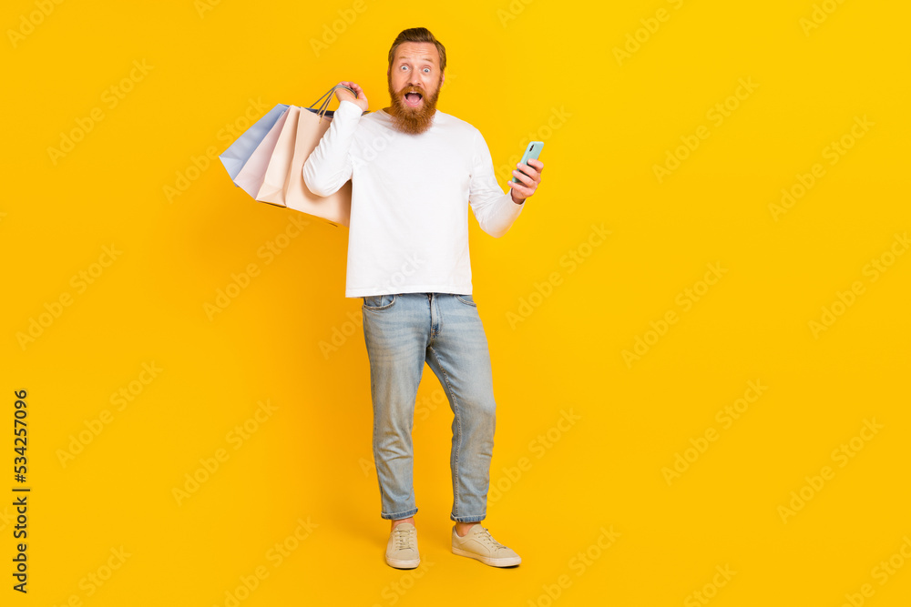 Full body photo of hooray beard man hold bags telephone wear white shirt jeans boots isolated on yellow color background Full body photo of hooray beard man hold bags telephone wear white shirt jeans boots isolated on yellow color background