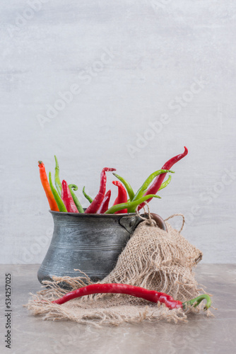 Old metal jug filled with red and green peppers on marble background