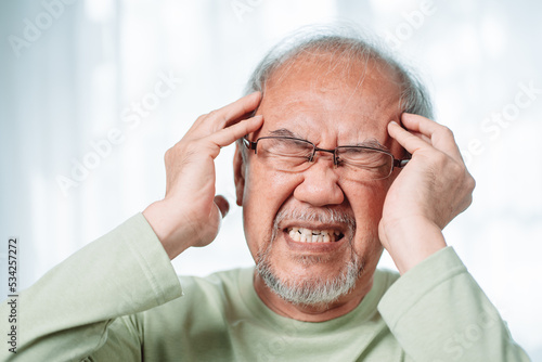 Closeup of Asian Senior elderly old man feel headache suffering and migraine in living room at home. Stressed mature male hurt mental health care and insurance concept.