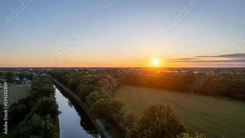 Colorful and dramatic sunset over the canal Dessel Schoten aerial photo shot by a drone in Rijkevorsel, kempen, Belgium, showing the waterway in the natural green agricultural landscape. High quality