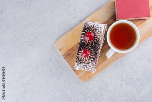 Slice of cake, cup of tea and book on wooden board