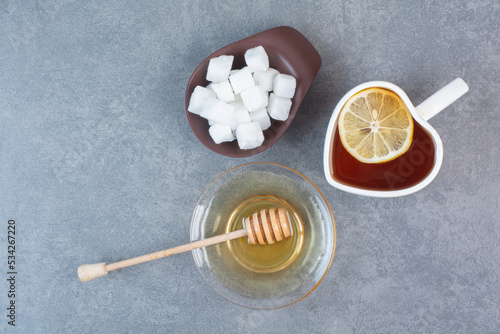 A cup of tea with sugar and honey on gray background