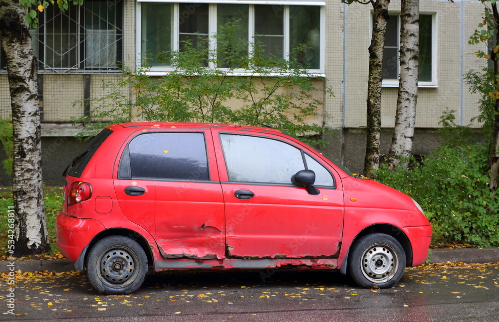 An old rusty broken red car is parked on the street, Iskrovsky Prospekt, St. Petersburg, Russia, September 2022