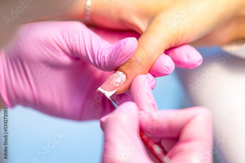 Nail design for a young girl or woman is drawn by a manicure master  a manicurist with a brush in a beauty salon. Nail care during manicure procedure.