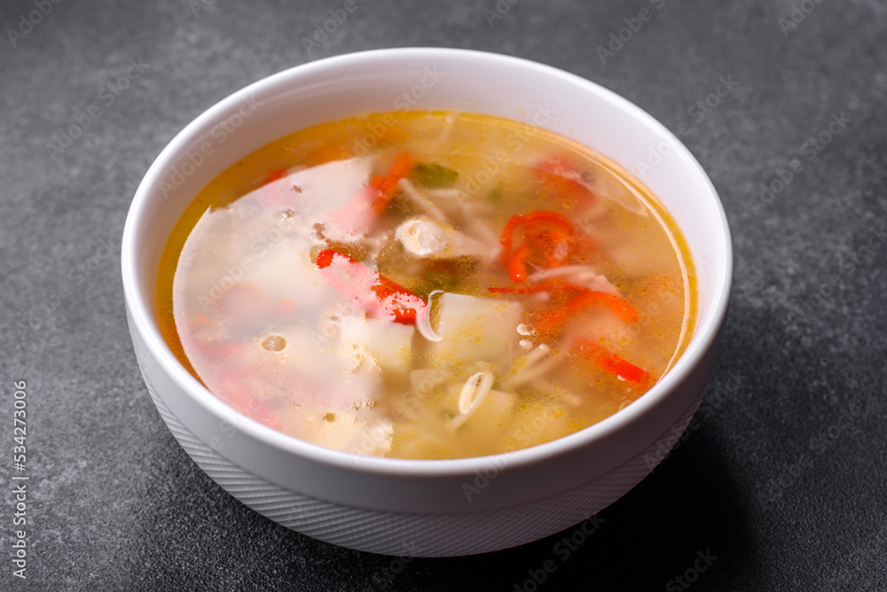 Closeup of a bowl of chicken noodle and vegetable soup on a concrete table Closeup of a bowl of chicken noodle and vegetable soup on a concrete table