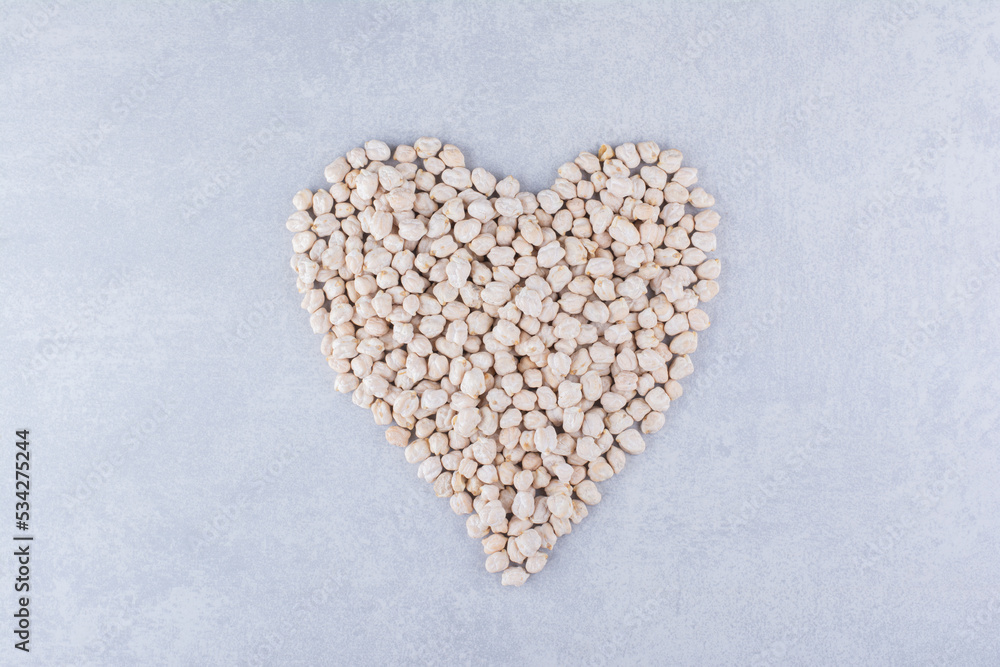 Small portion of chickpeas arranged into a heart shape on marble background