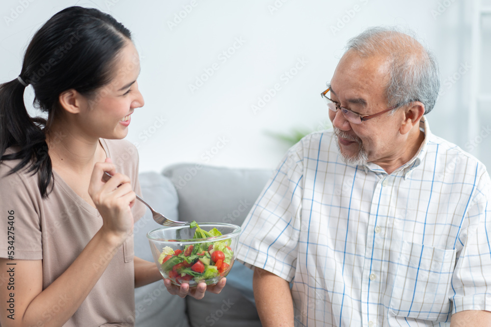 Young Asian daughter serving and feeding food to senior father in the living room. family love and support to patient grandfather. take care happy old man at home. Young Asian daughter serving and feeding food to senior father in the living room. family love and support to patient grandfather. take care happy old man at home.