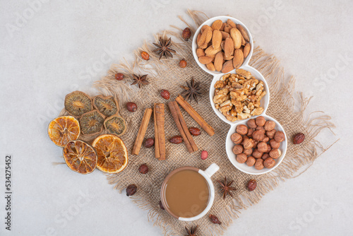 A cup of coffee with dried oranges and nuts on marble background