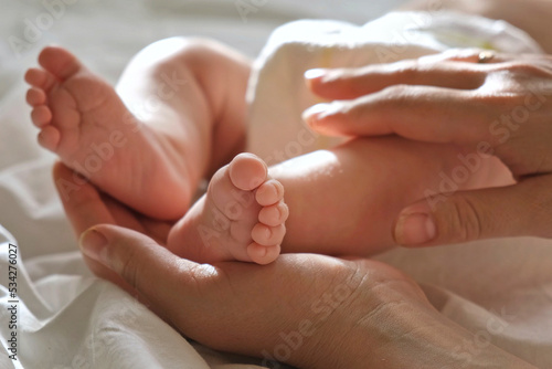 Baby feet in mother hands, on her palm. Happy parents holding their baby feet, close up. Maternity, family, birth concept. Woman touching legs of infant baby. Tiny foot of newborn. Mom and her Child.