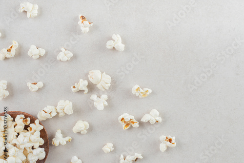 Popcorn piled on a small wooden saucer and scattered around on marble background
