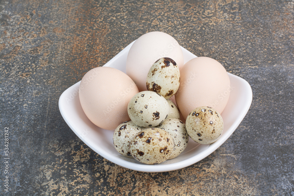 Chicken and quail eggs on white bowl Chicken and quail eggs on white bowl