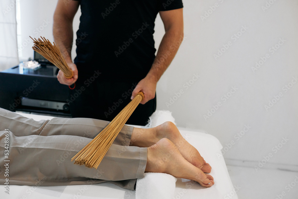 Bamboo brooms in masseur hands in motion while massaging legs of